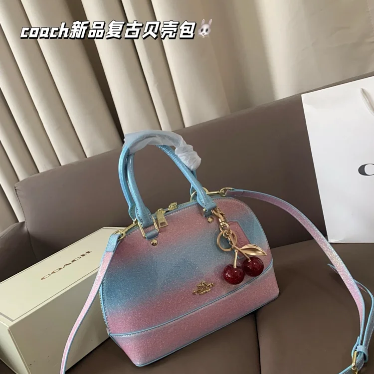 Coach Mini Sierra Satchel handbag with a gradient pink and blue design and a cherry bag charm.