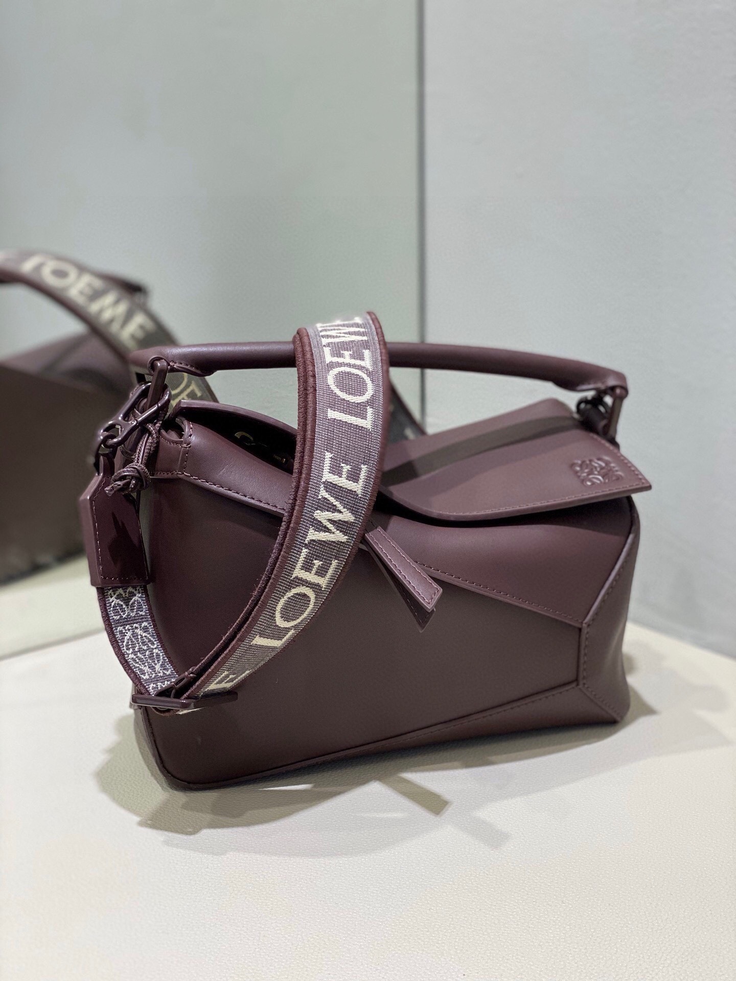 Loewe Puzzle bag in a brown or burgundy leather, featuring a logo-emblazoned shoulder strap