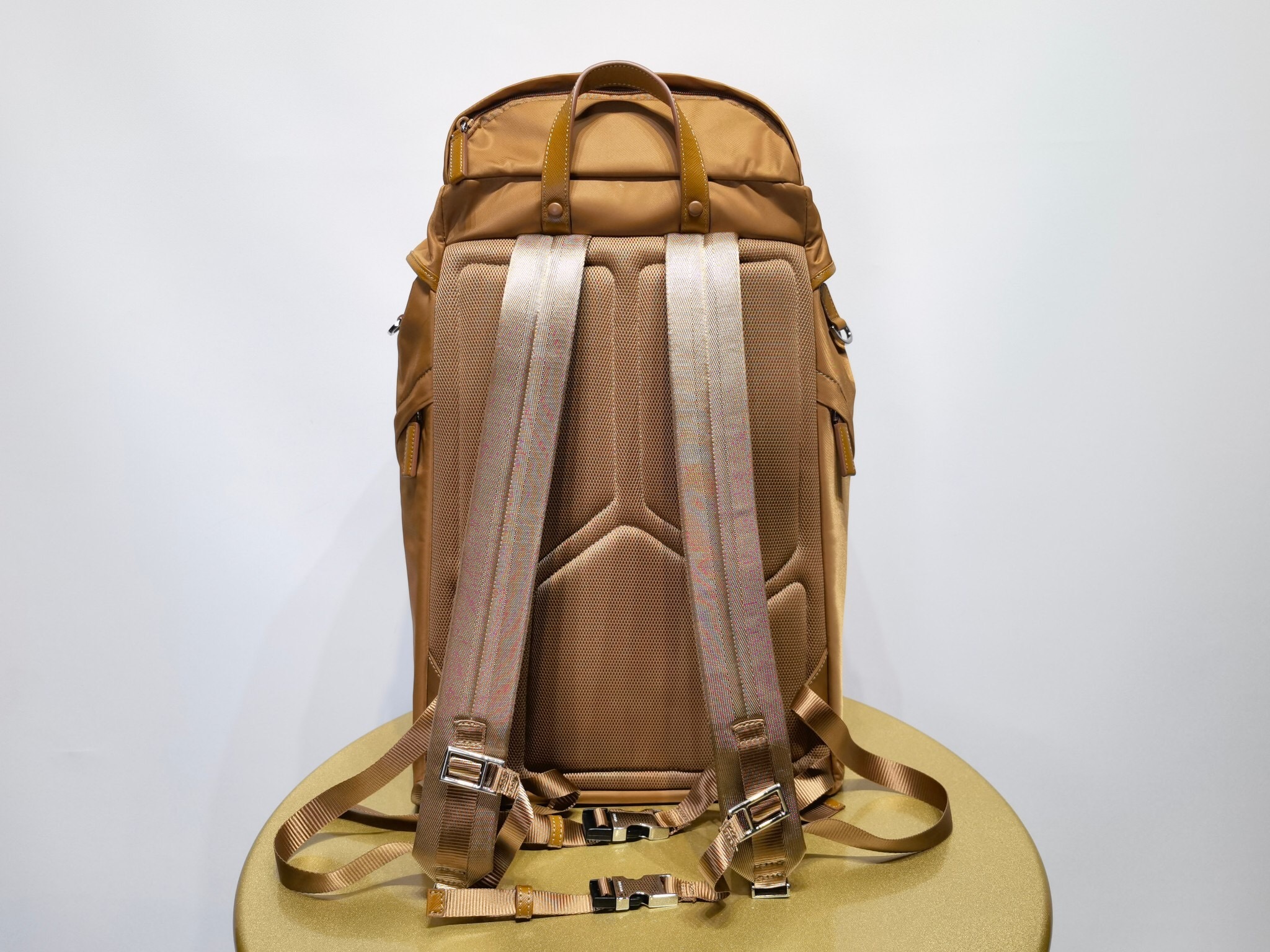 Prada Re-Nylon backpack in a tobacco or brown color iconic enameled metal triangle logo plaque on the flap with side-release buckles, and external flap pockets
