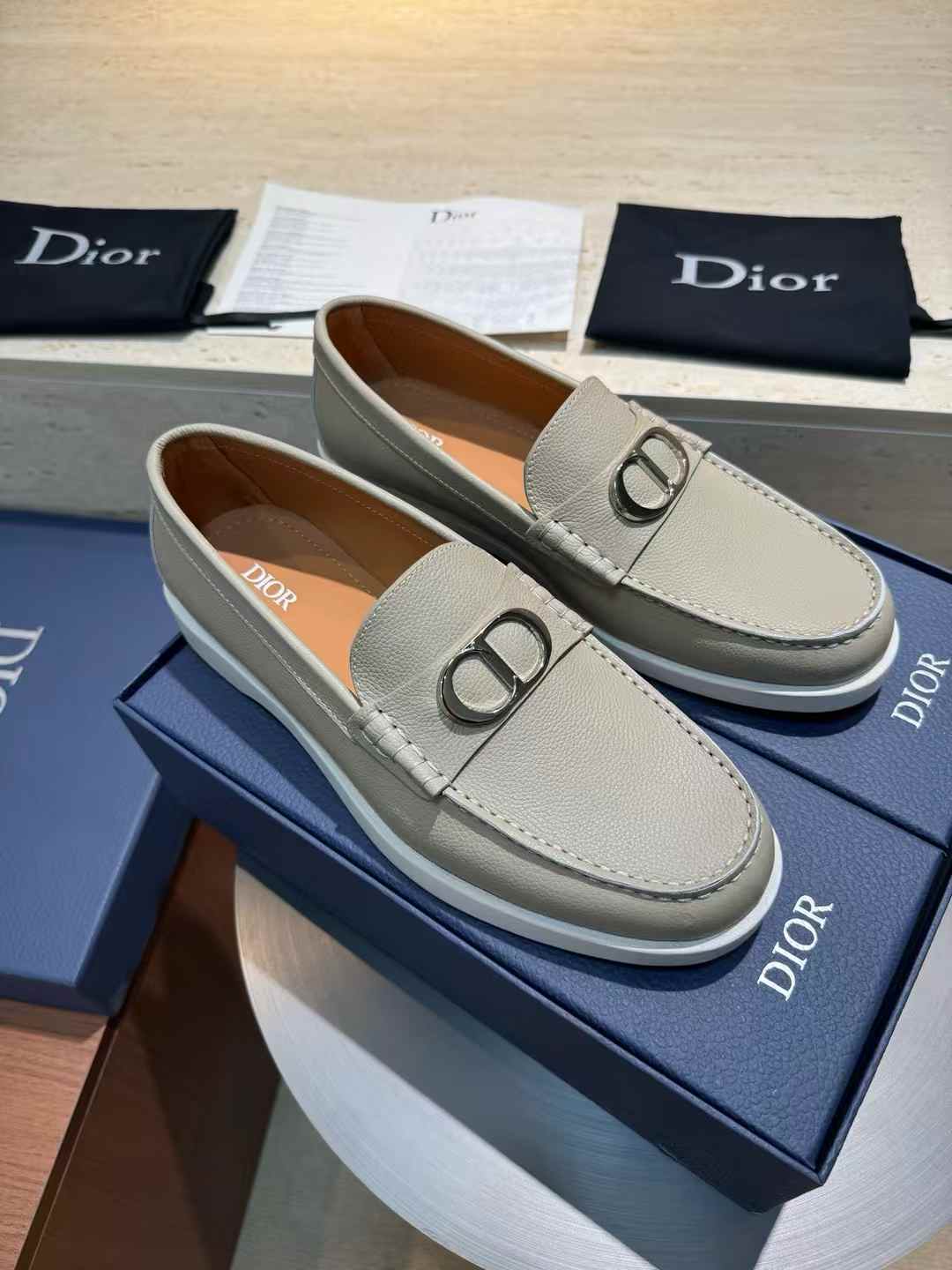 Dior Granville loafers in a gray suede or leather material with a white rubber sole and a palladium-finish brass "CD Icon" buckle on the vamp