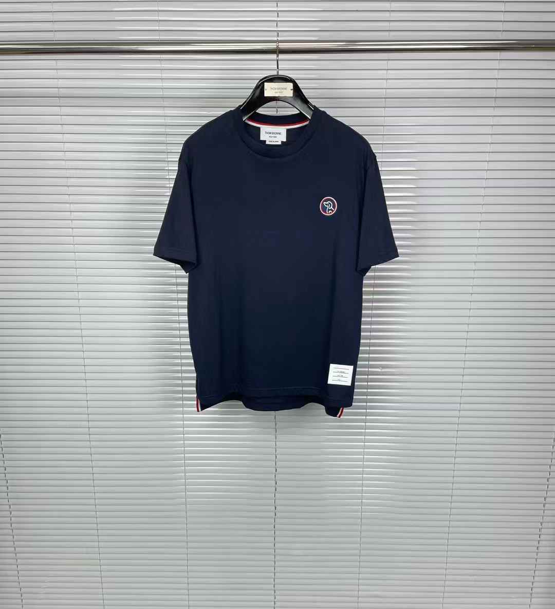Thom Browne t-shirt with a small logo patch on the chest and the brand's signature red, white, and blue grosgrain trim on the sleeves and hem