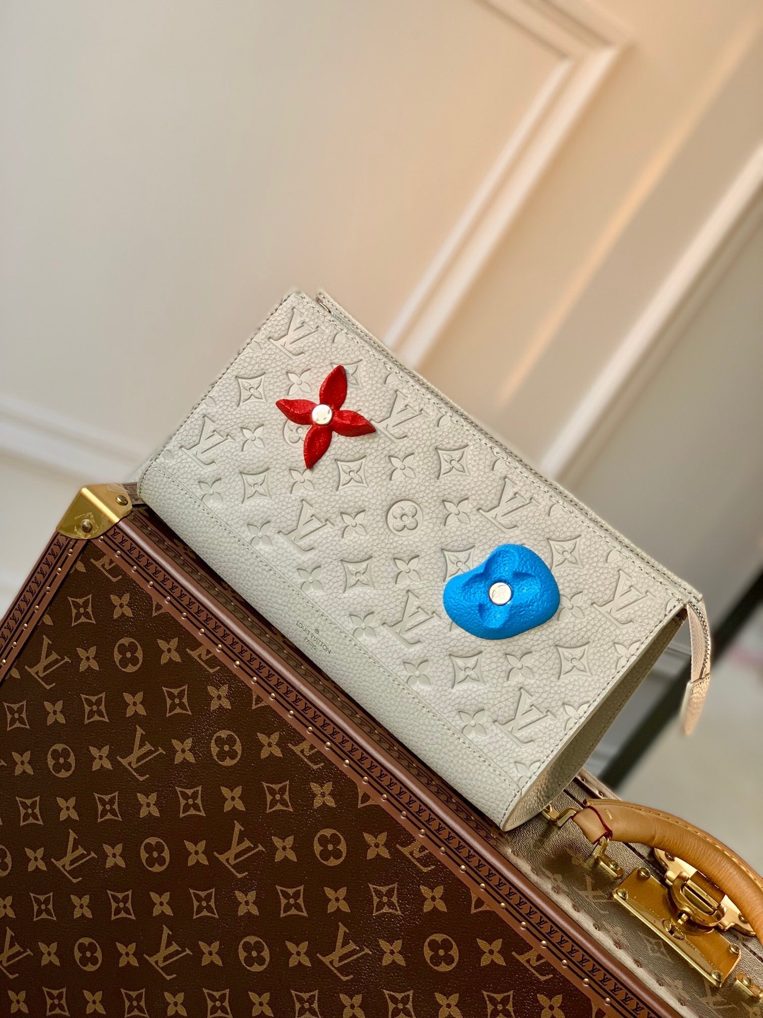 LV Sac Tricot wallet in a light-colored monogram canvas with a red flower and a blue heart embellishment.