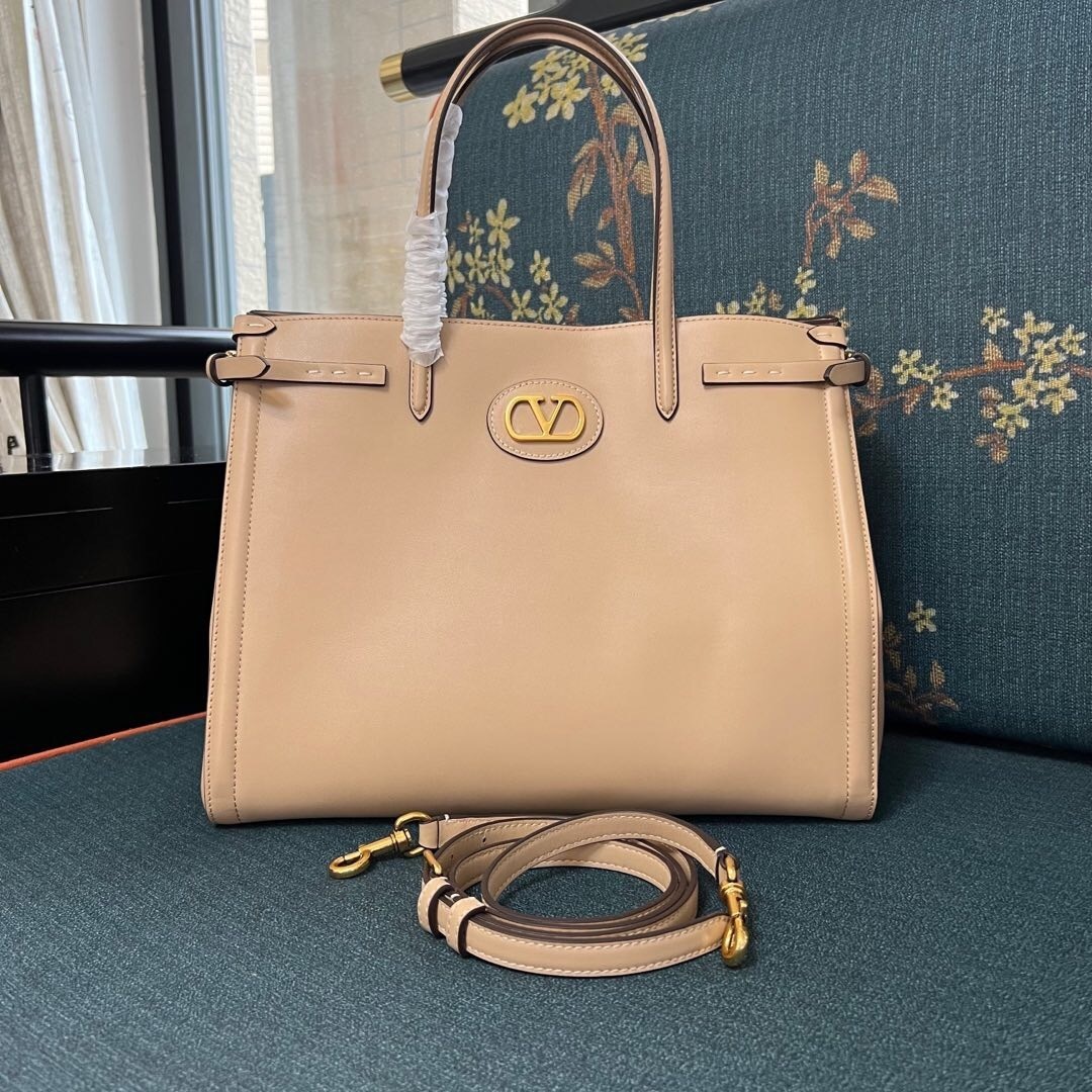 Valentino Garavani Antibes medium leather tote bag in a light neutral color, detailed with side buckles and a VLogo Signature metal feature