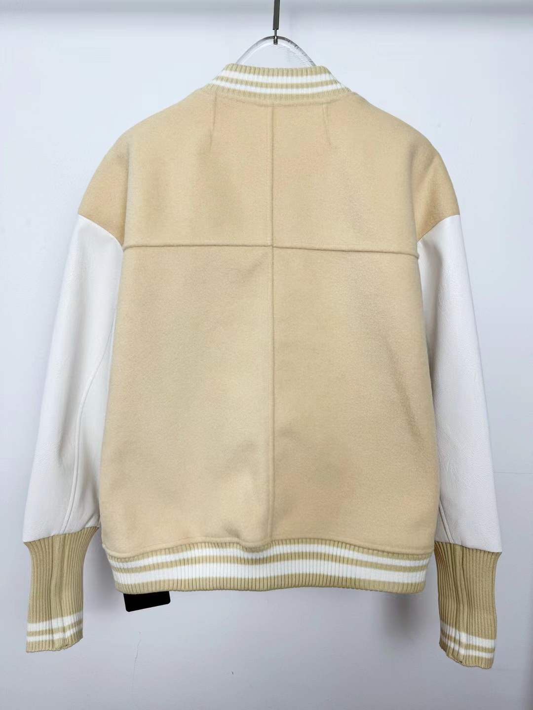 LV varsity jacket beige wool body, white leather sleeves, and a graphic bird patch and "LV" lettering on the chest