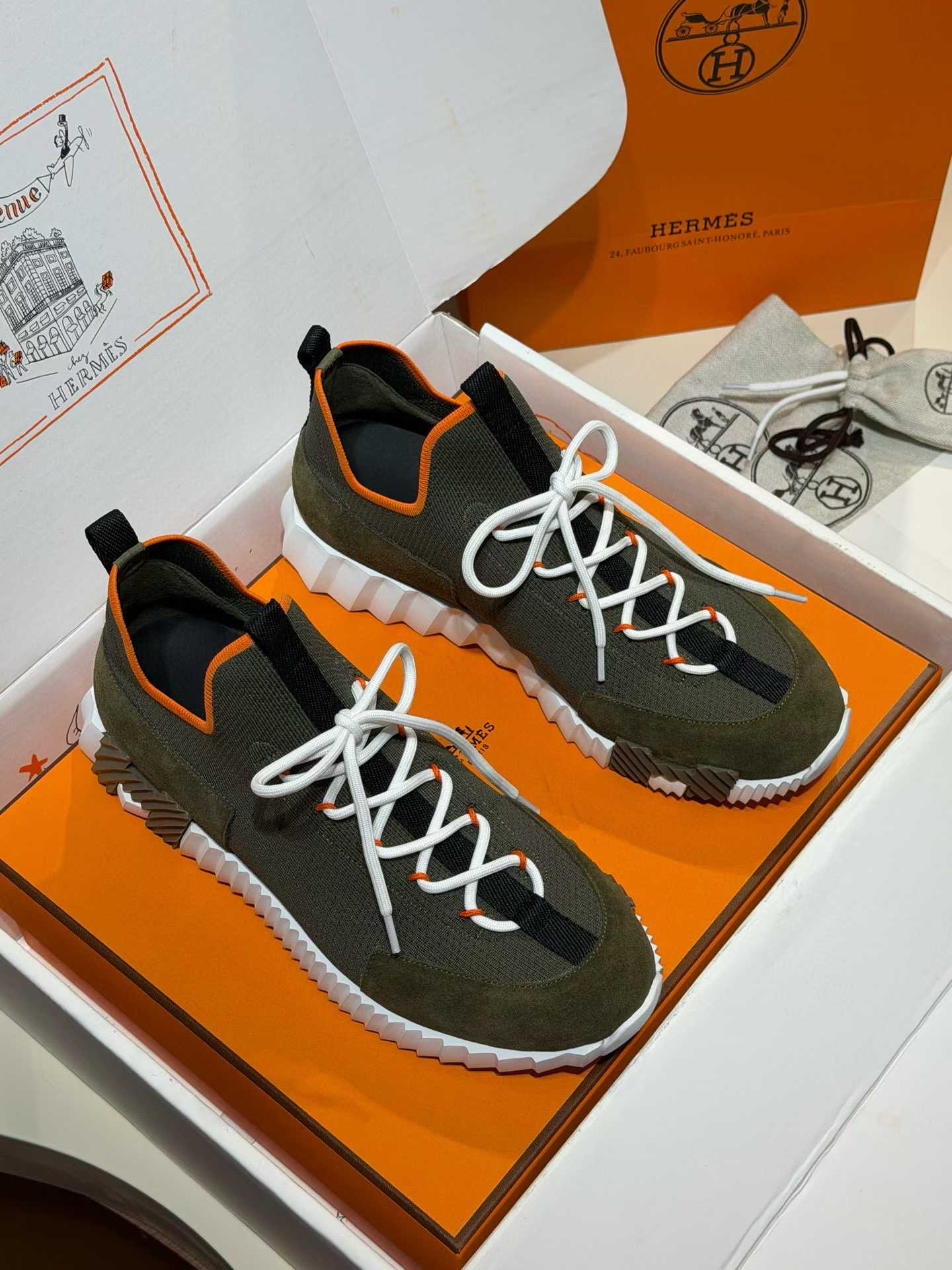 Hermès Lift slip-on sneakers in a dark olive or navy color with white laces and an orange trim