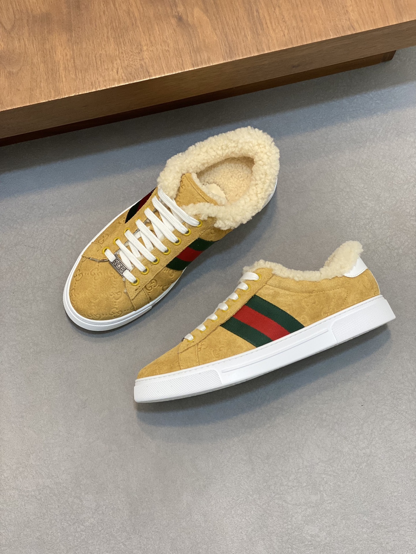 Gucci Ace low-top sneaker in a tan suede finish with a sheep fur lining and the signature green and red Web stripe on the sides.