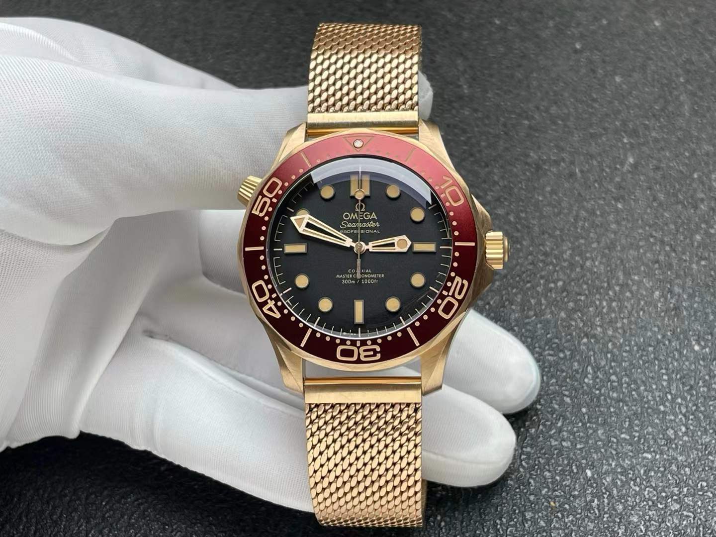 Seamaster Diver 300M Co-Axial Master Chronometer 42 mm watch in bronze gold with a burgundy red bezel and black dial, presented on a bronze gold mesh bracelet