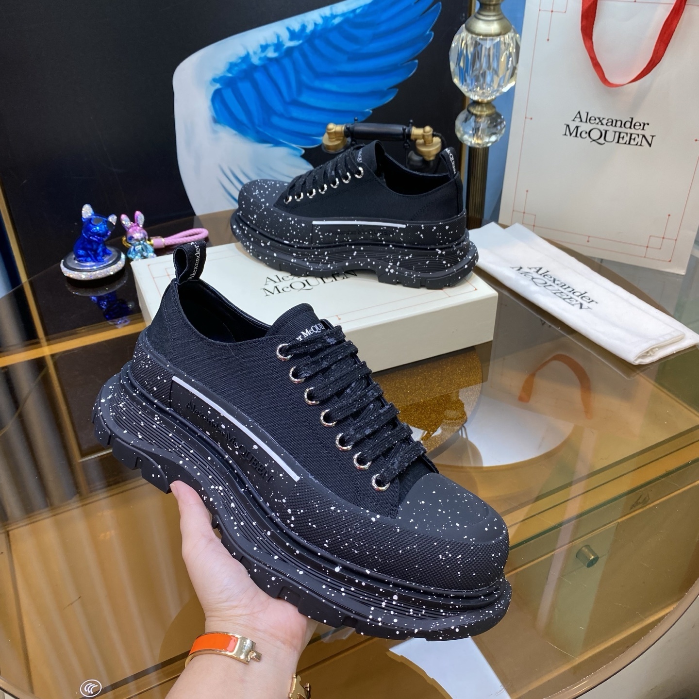 Alexander McQueen Tread Slick Lace Up sneaker with a black canvas upper and a white paint splatter detail on the chunky rubber tread sole