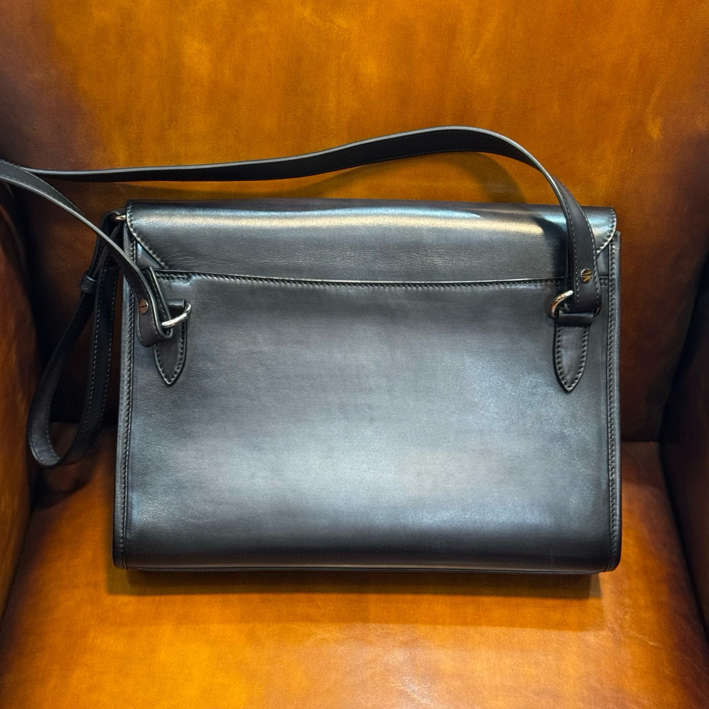 black leather satchel bag with a top handle, shoulder strap, and metallic turn-lock closure.