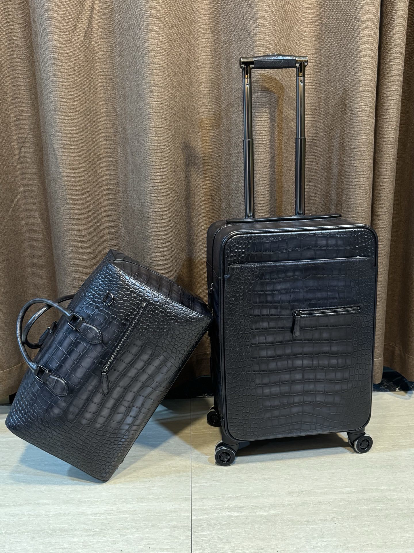 Berluti black crocodile-embossed leather luggage set including a wheeled suitcase and a duffel bag.