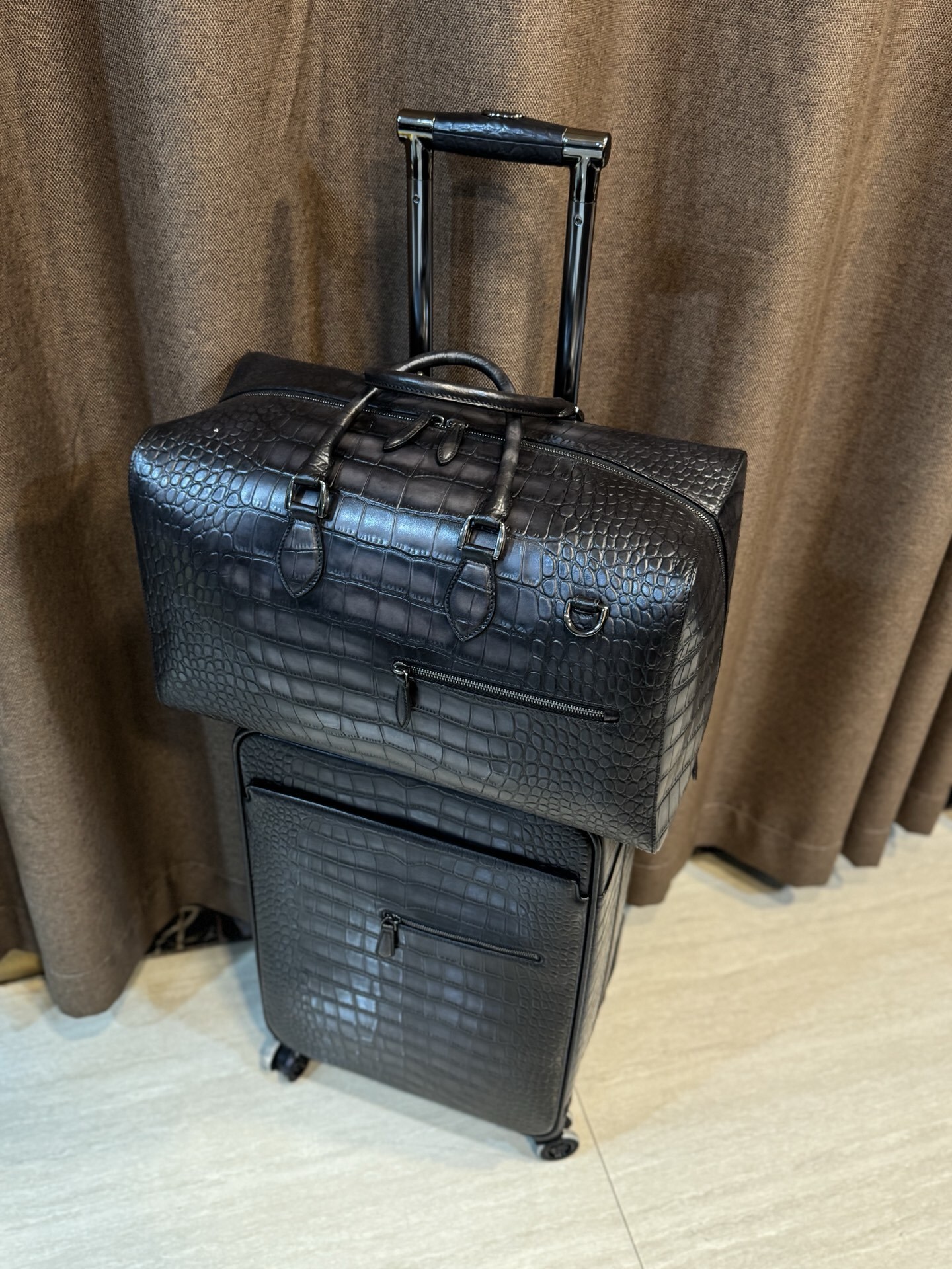 Berluti black crocodile-embossed leather luggage set including a wheeled suitcase and a duffel bag.