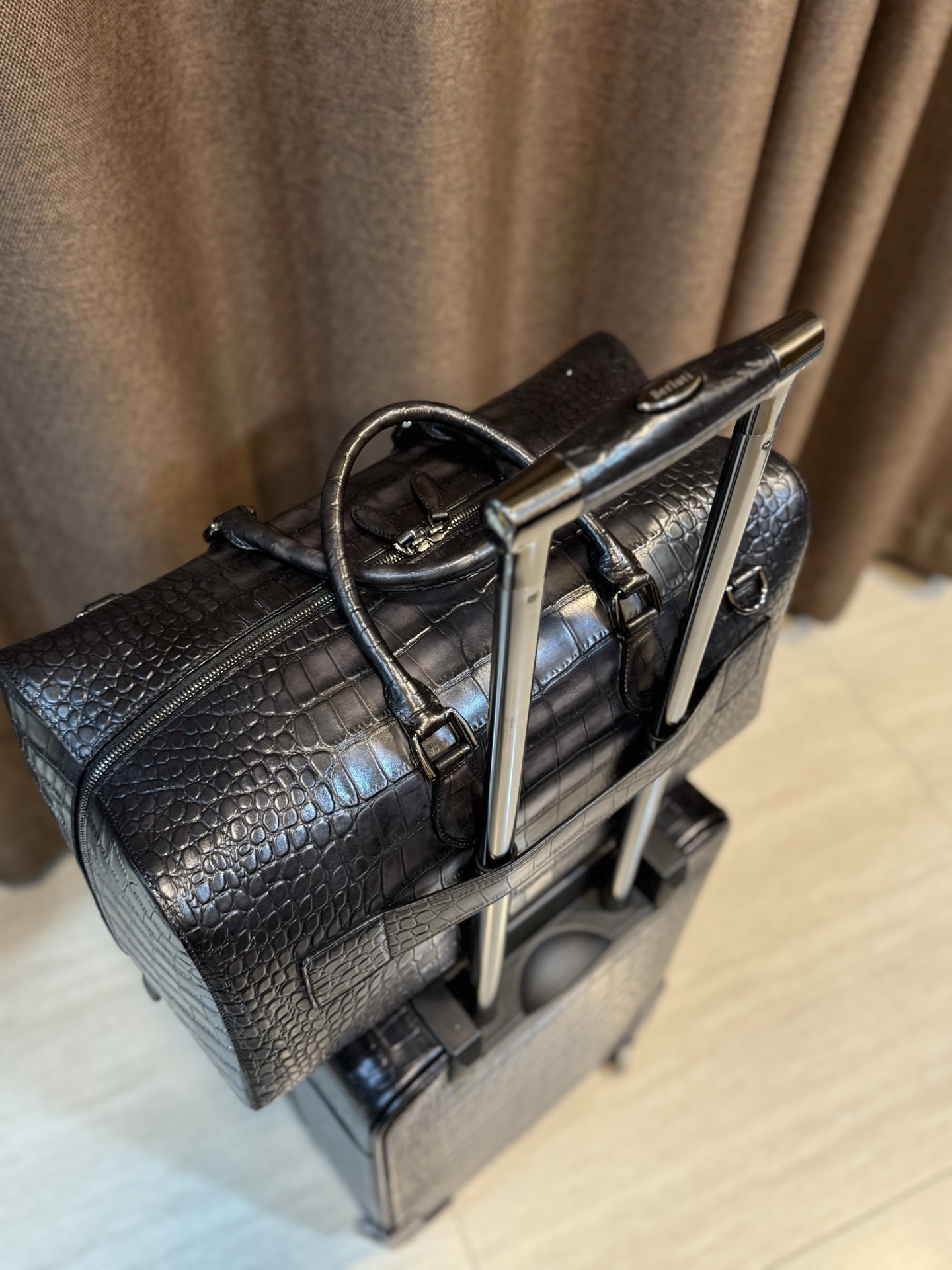Berluti black crocodile-embossed leather luggage set including a wheeled suitcase and a duffel bag.