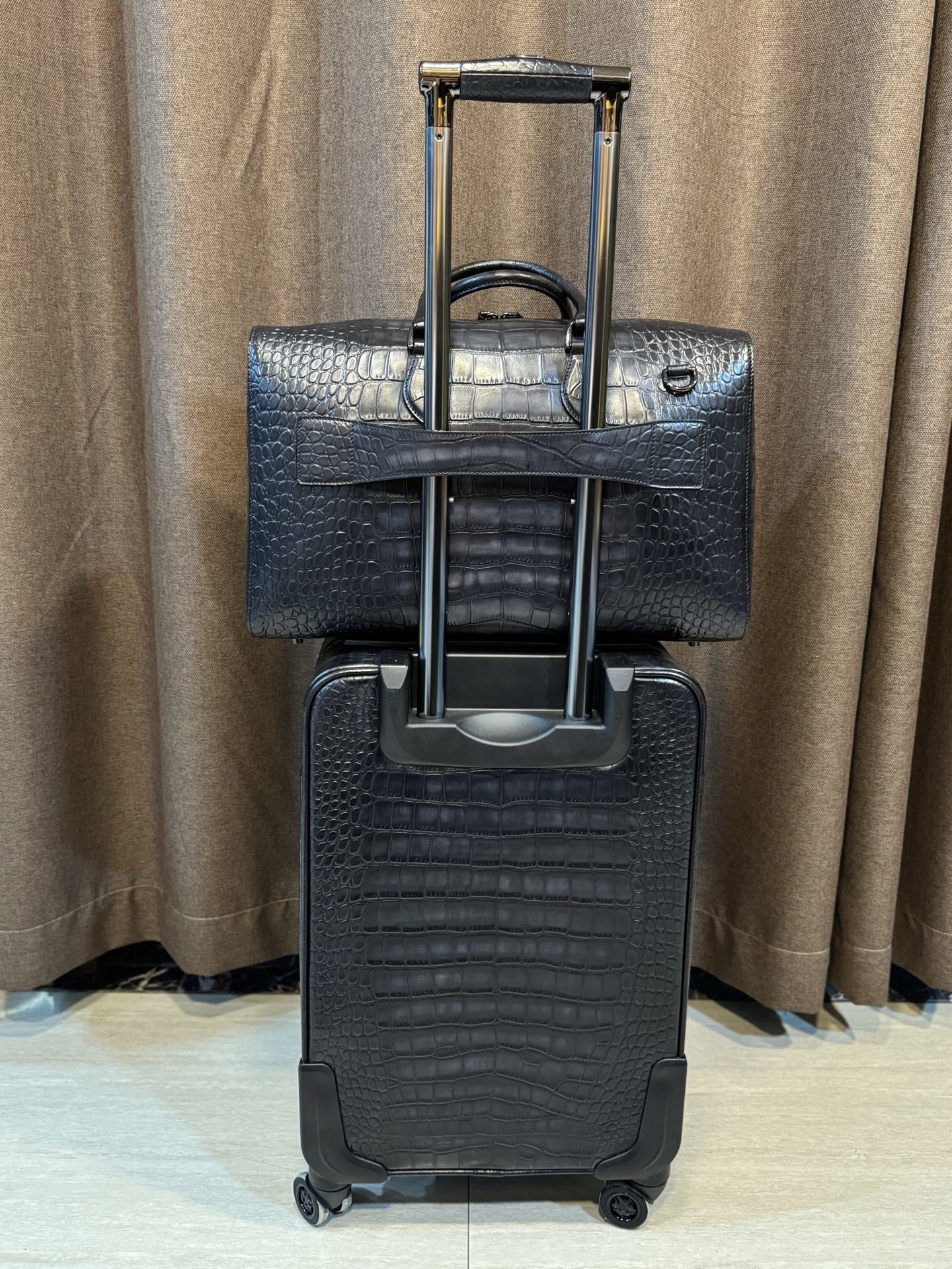 Berluti black crocodile-embossed leather luggage set including a wheeled suitcase and a duffel bag.