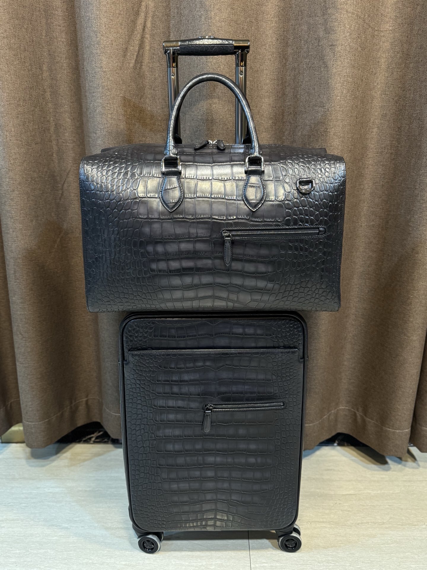 Berluti black crocodile-embossed leather luggage set including a wheeled suitcase and a duffel bag.