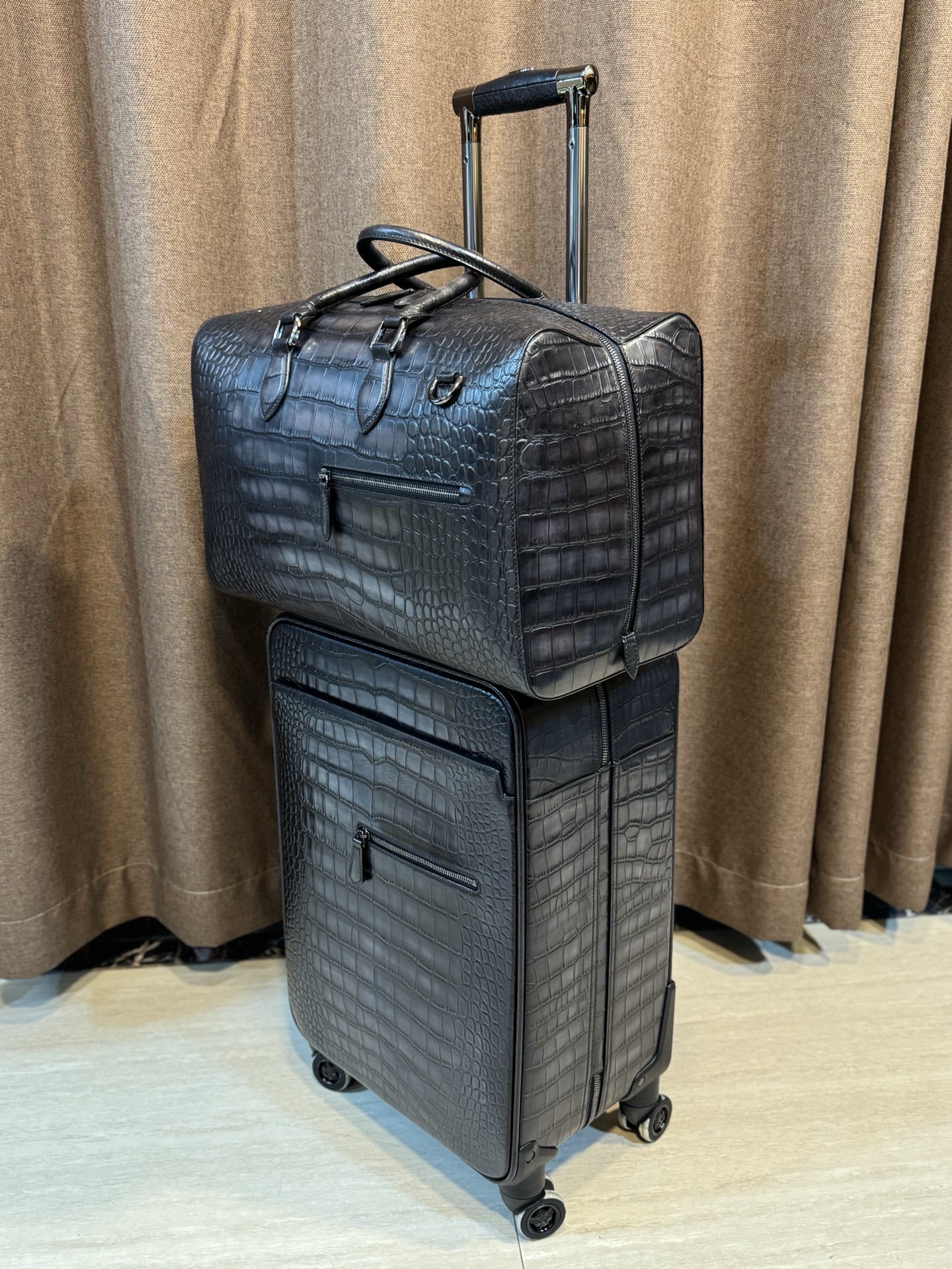 Berluti black crocodile-embossed leather luggage set including a wheeled suitcase and a duffel bag.