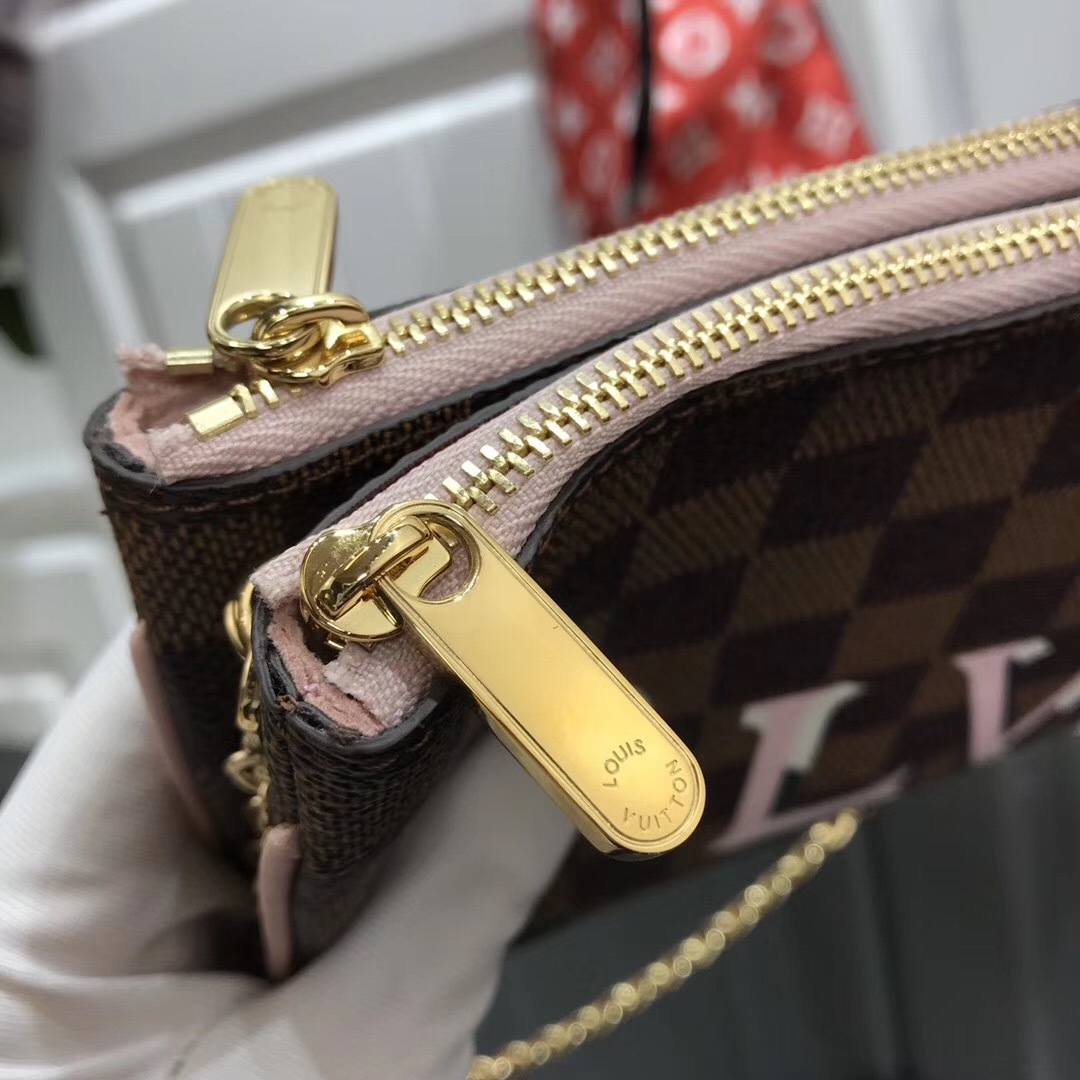 LV Damier Ebene Double Zip Pochette in Pink is a versatile crossbody bag crafted from the iconic checkerboard canvas, featuring distinctive pink leather trim and a prominent LV signature.