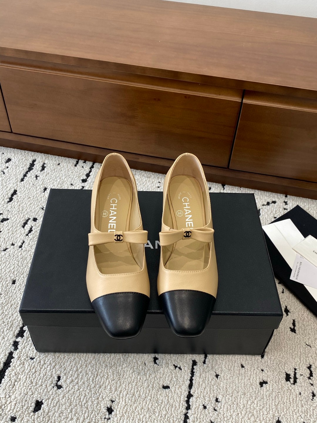 Chanel Mary Jane heels are designed in a classic two-tone beige and black leather style with a sturdy block heel and a ribbon strap detail.