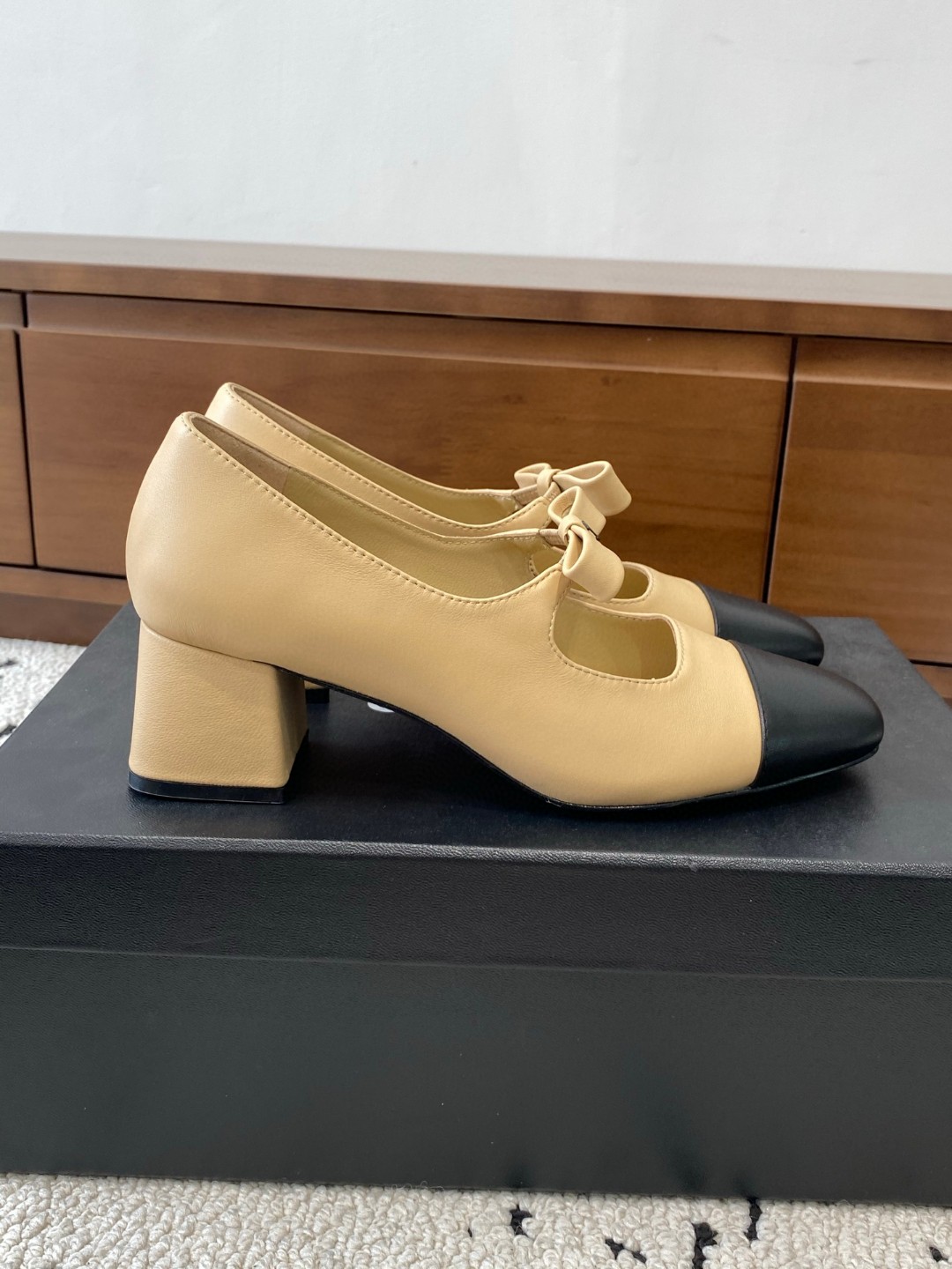Chanel Mary Jane heels are designed in a classic two-tone beige and black leather style with a sturdy block heel and a ribbon strap detail.