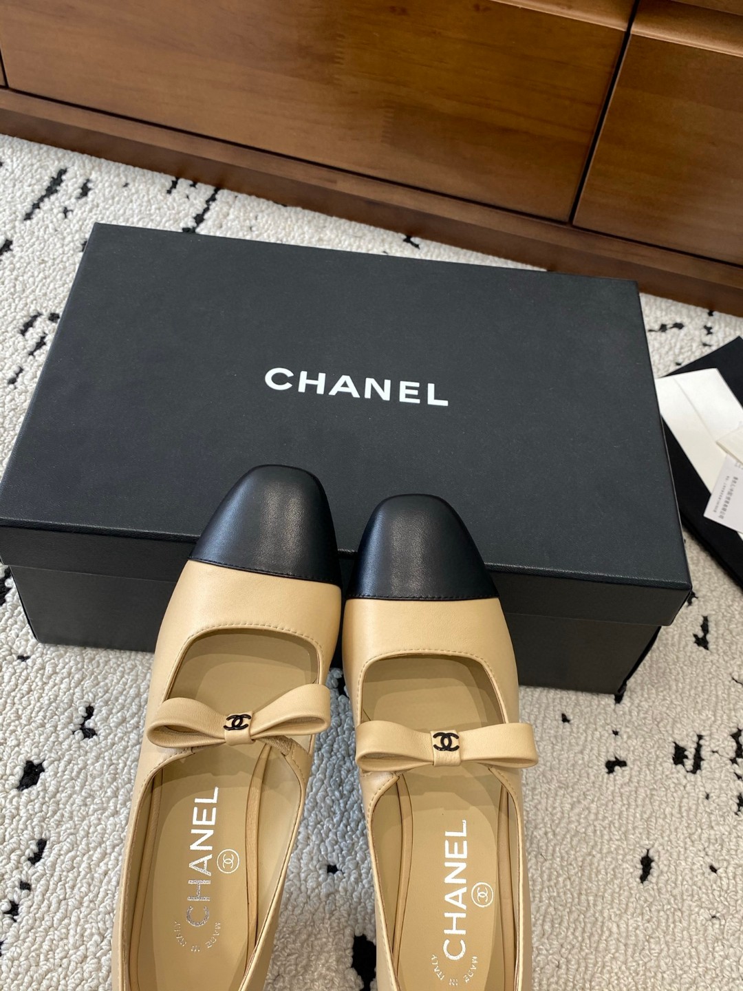 Chanel Mary Jane heels are designed in a classic two-tone beige and black leather style with a sturdy block heel and a ribbon strap detail.