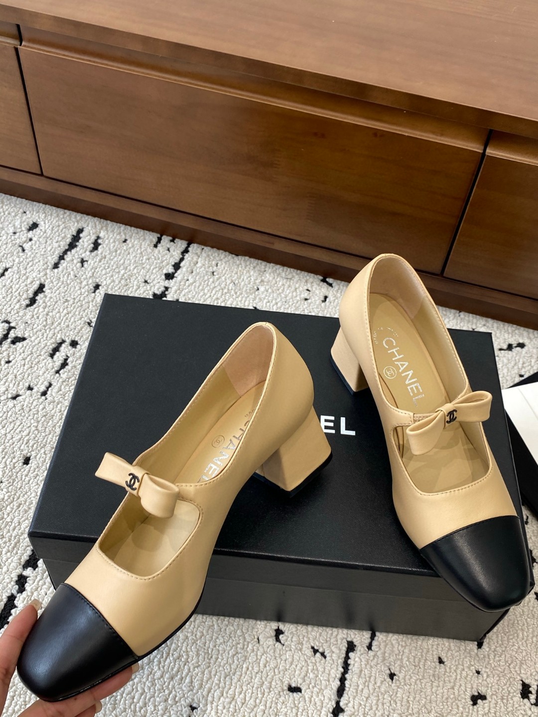 Chanel Mary Jane heels are designed in a classic two-tone beige and black leather style with a sturdy block heel and a ribbon strap detail.