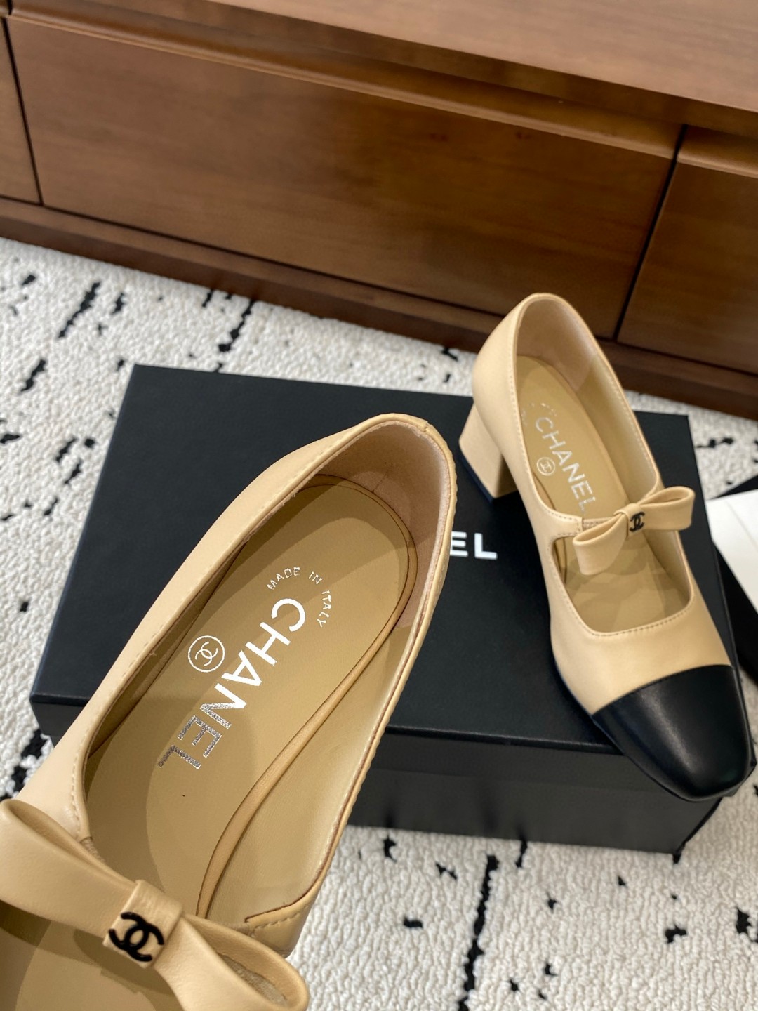 Chanel Mary Jane heels are designed in a classic two-tone beige and black leather style with a sturdy block heel and a ribbon strap detail.