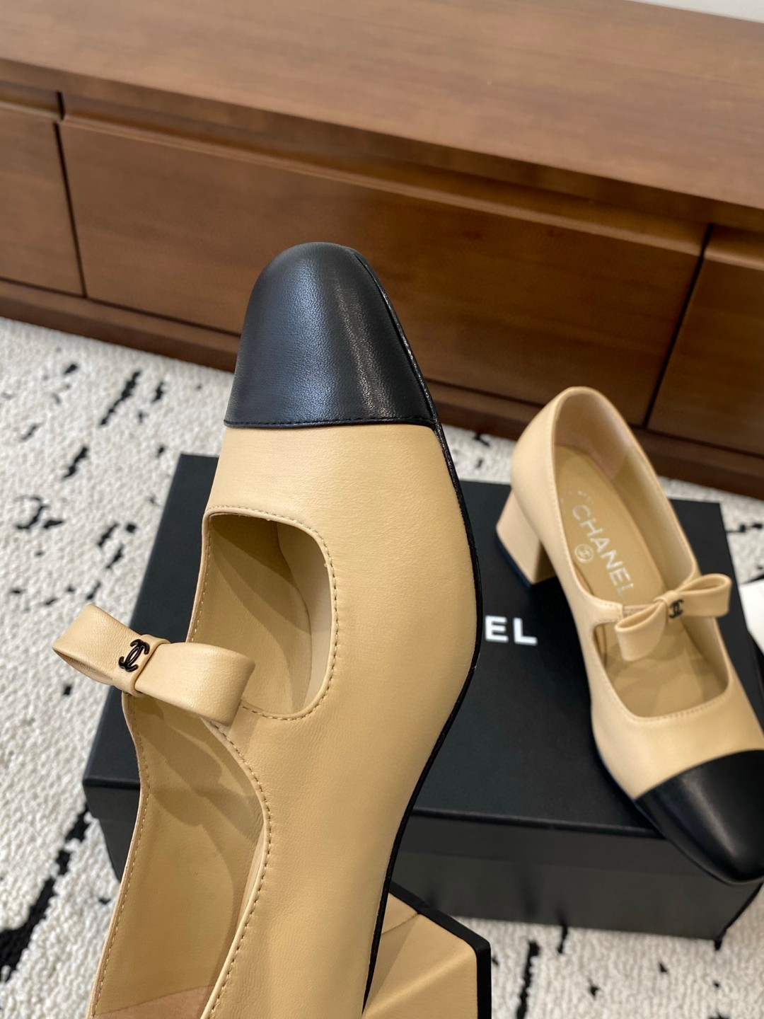 Chanel Mary Jane heels are designed in a classic two-tone beige and black leather style with a sturdy block heel and a ribbon strap detail.