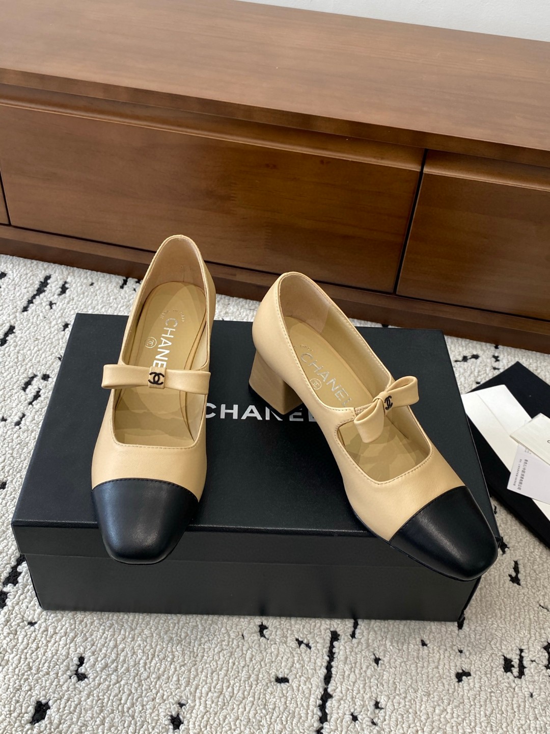 Chanel Mary Jane heels are designed in a classic two-tone beige and black leather style with a sturdy block heel and a ribbon strap detail.