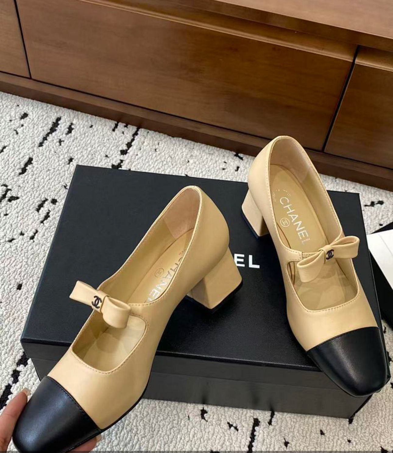Chanel Mary Jane heels are designed in a classic two-tone beige and black leather style with a sturdy block heel and a ribbon strap detail.