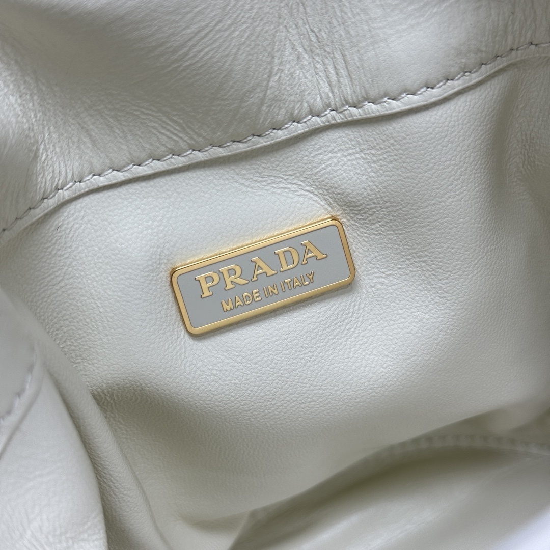 Prada Petit Sac Noir mini bucket bag is crafted from white nappa leather and features a gold-tone chain closure, a matching top handle, and a metallic sphere charm