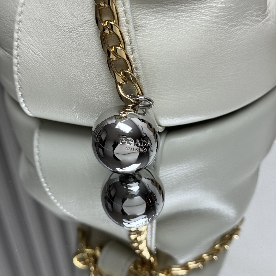 Prada Petit Sac Noir mini bucket bag is crafted from white nappa leather and features a gold-tone chain closure, a matching top handle, and a metallic sphere charm