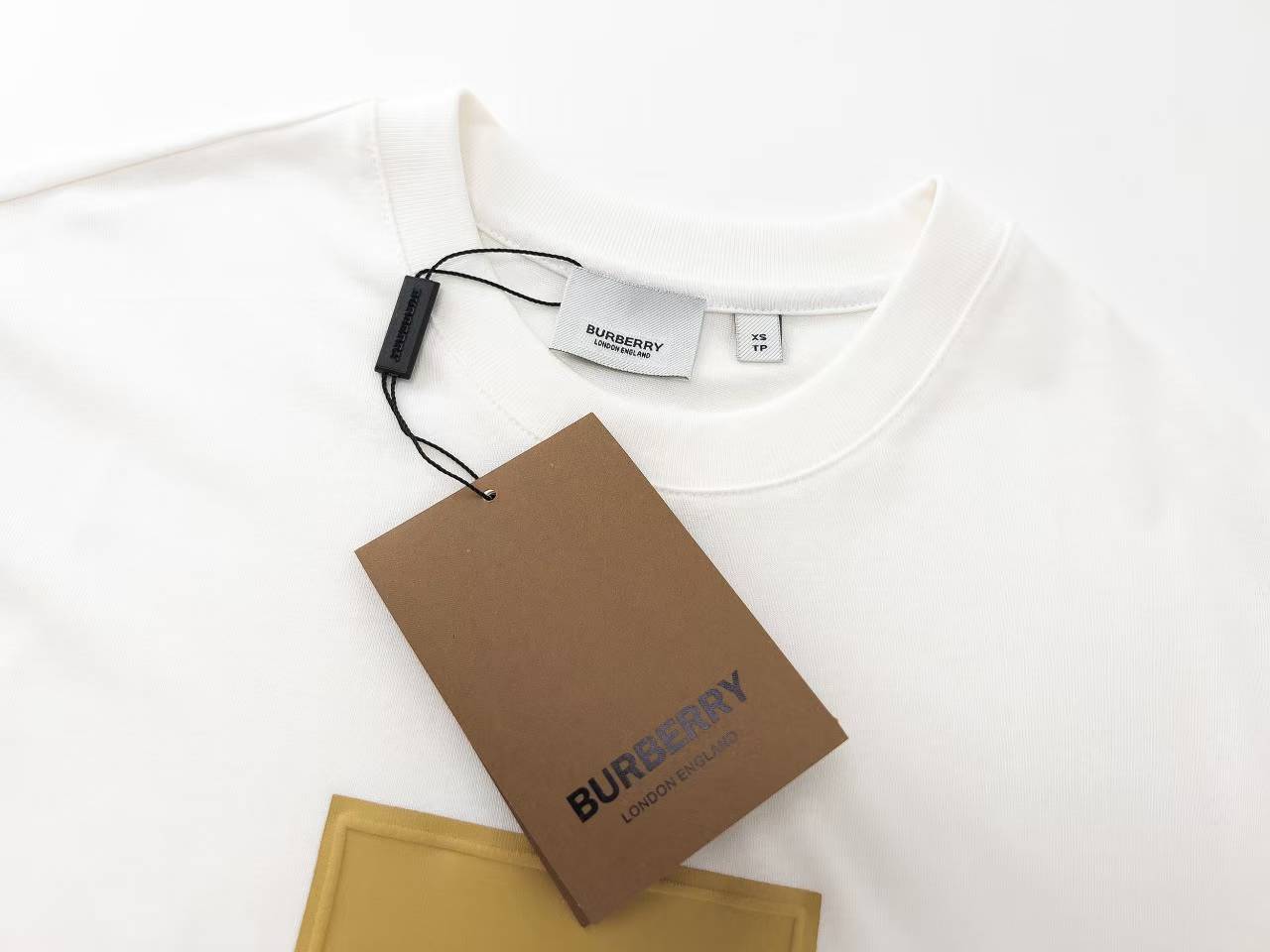 Burberry Label Appliqué Cotton Oversized T-Shirt is a white cotton t-shirt featuring a distinctive woven patch inspired by signature trench coat labels.