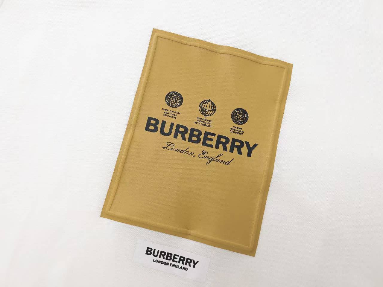 Burberry Label Appliqué Cotton Oversized T-Shirt is a white cotton t-shirt featuring a distinctive woven patch inspired by signature trench coat labels.