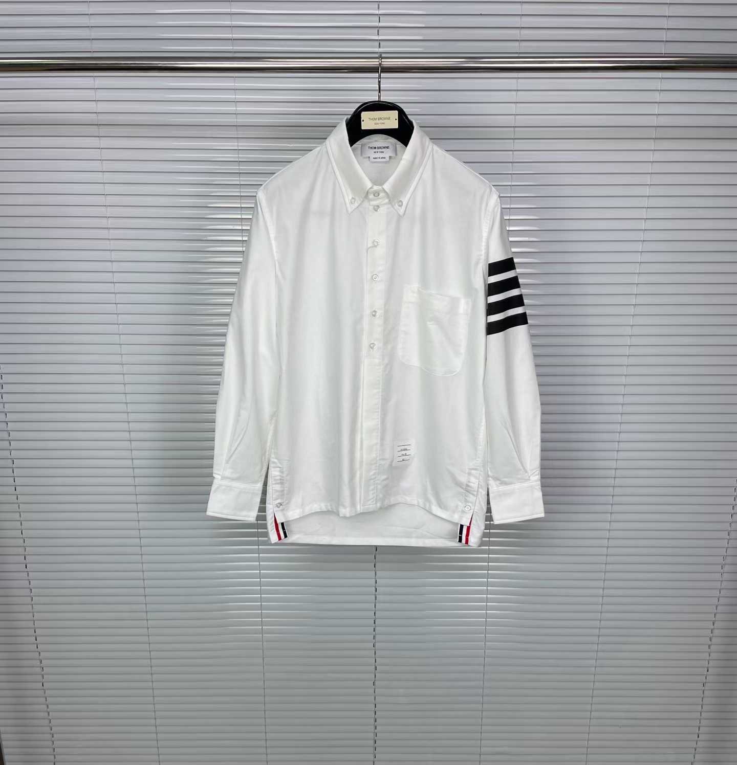 Thom Browne white cotton button-down shirt featuring the signature 4-bar stripe detail on the left sleeve.