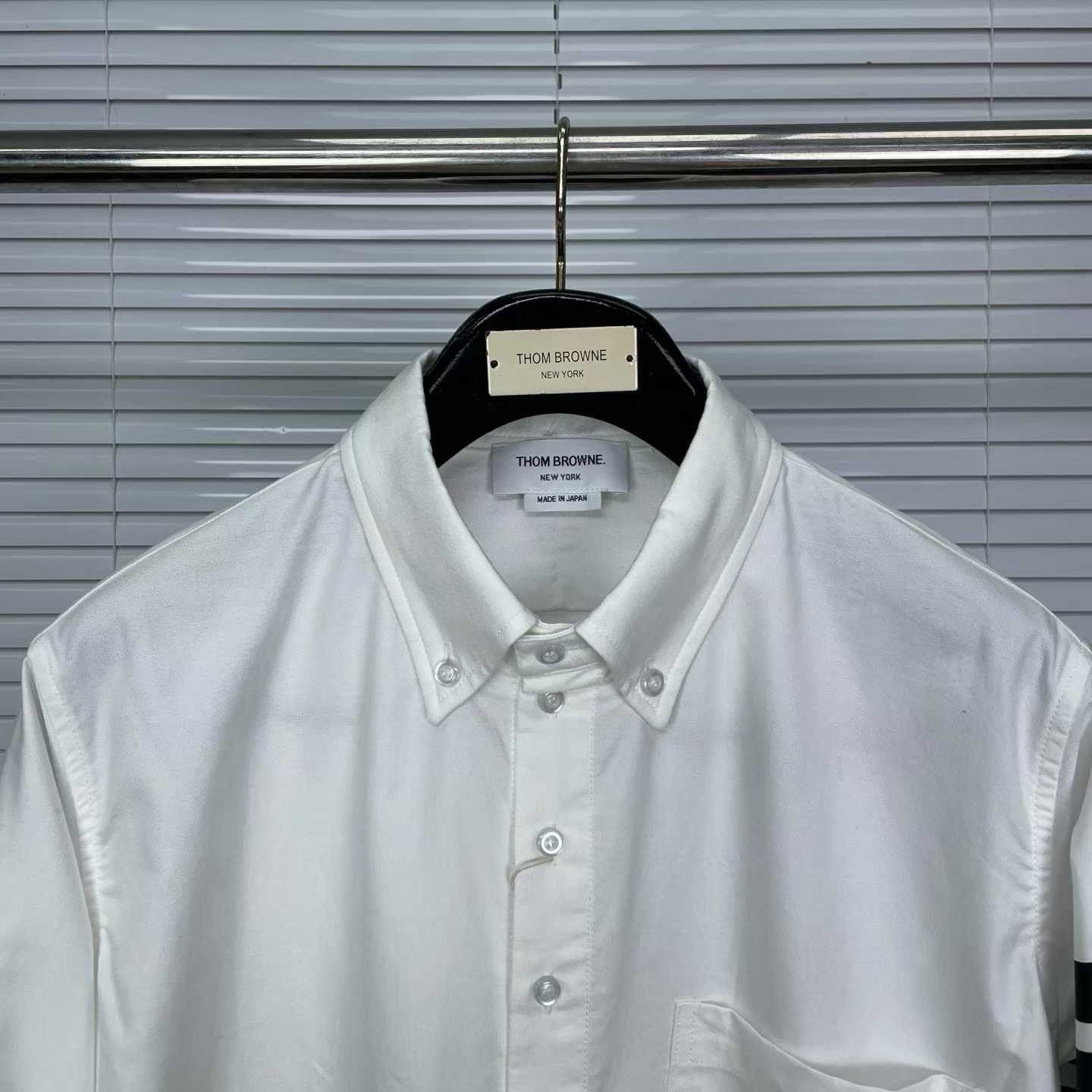 Thom Browne white cotton button-down shirt featuring the signature 4-bar stripe detail on the left sleeve.