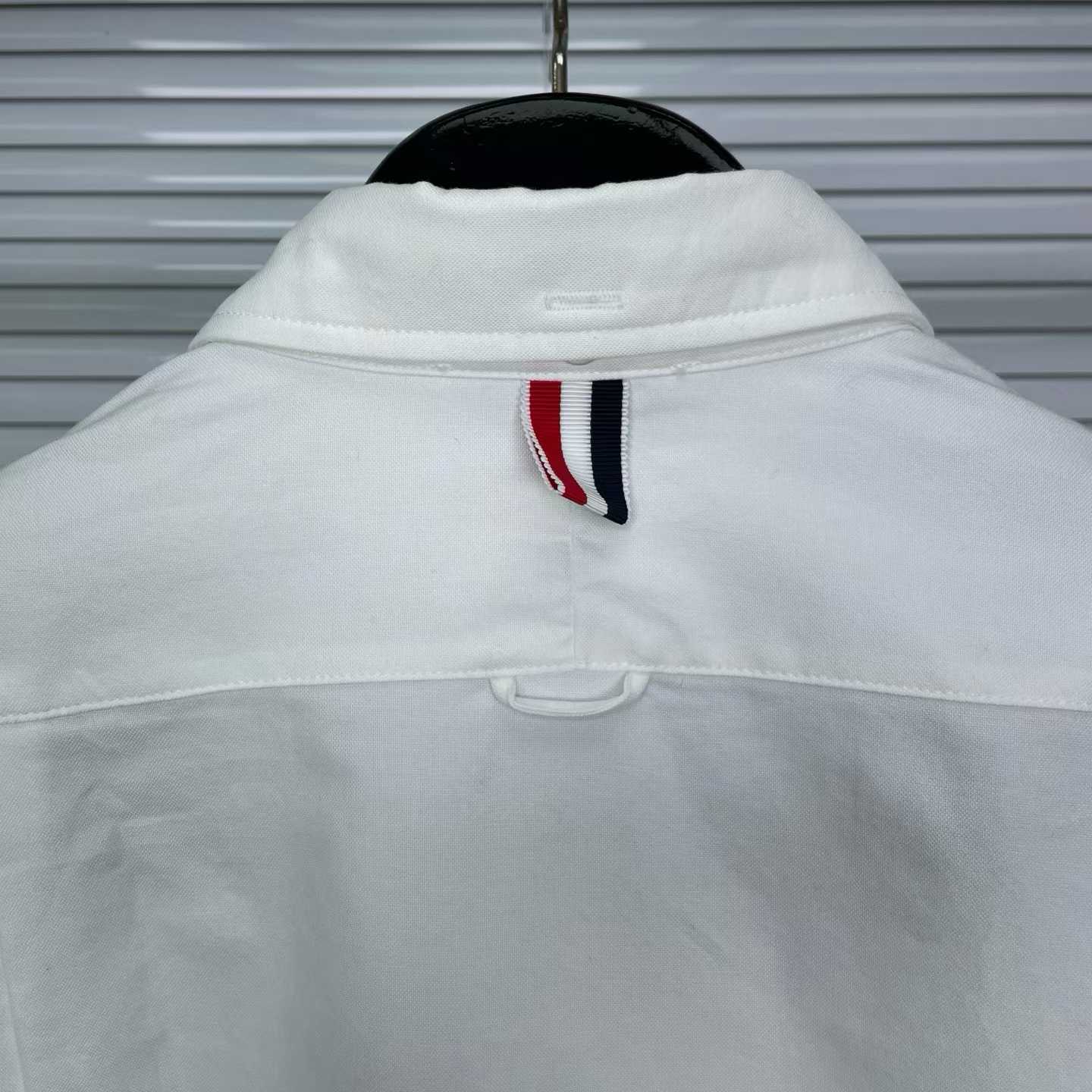 Thom Browne white cotton button-down shirt featuring the signature 4-bar stripe detail on the left sleeve.